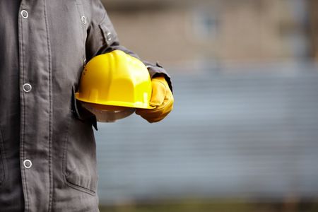 A construction worker is holding a yellow hard hat in his hands.