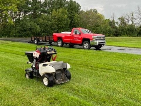 a lawn mower is parked next to a red truck on a lush green field.