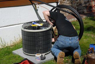 Man wearing black repairing A/C unit outdoors