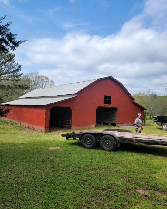 A man is pushing a trailer in front of a red barn.