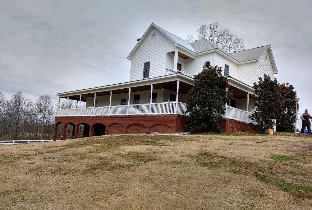 A large white house with a large porch sits on top of a grassy hill.