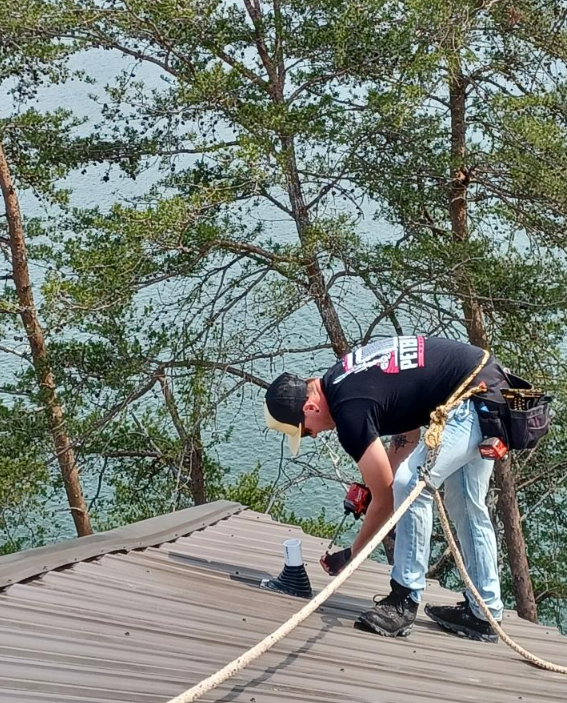 A man is working on a roof with trees in the background.