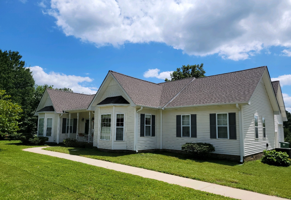 A white house with a brown roof and black shutters on a sunny day.