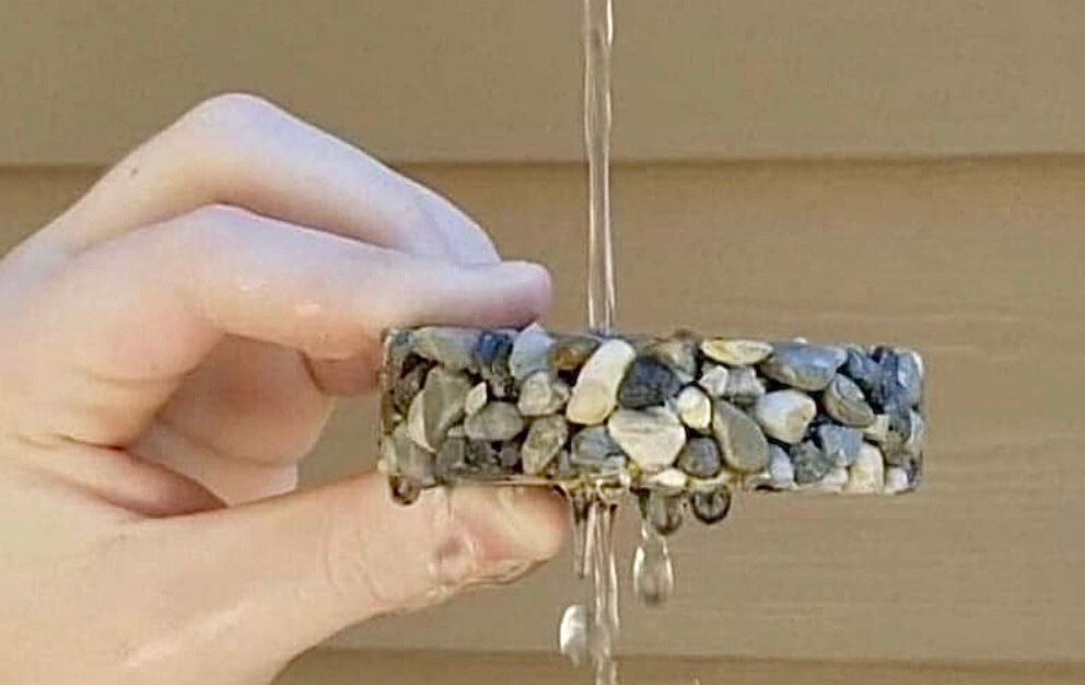Hand holding a stone-covered object, water pouring through it and dripping down.