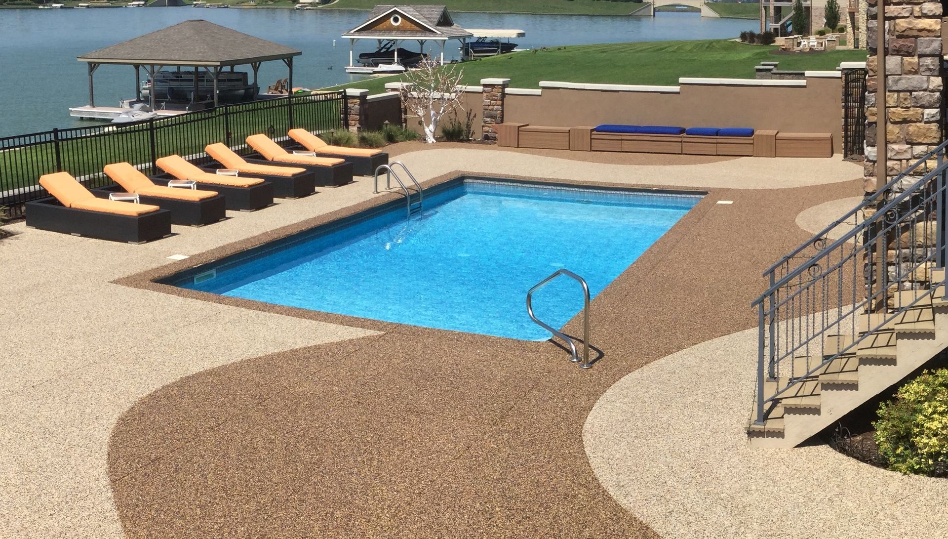 Poolside patio overlooking a lake, with lounge chairs, a rectangular pool, and a stairway.