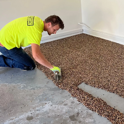 A person spreads a brown epoxy floor coating in a garage, using a trowel.