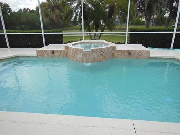 A backyard swimming pool with a raised stone-tiled spa spilling into the water, enclosed by a screen lanai.