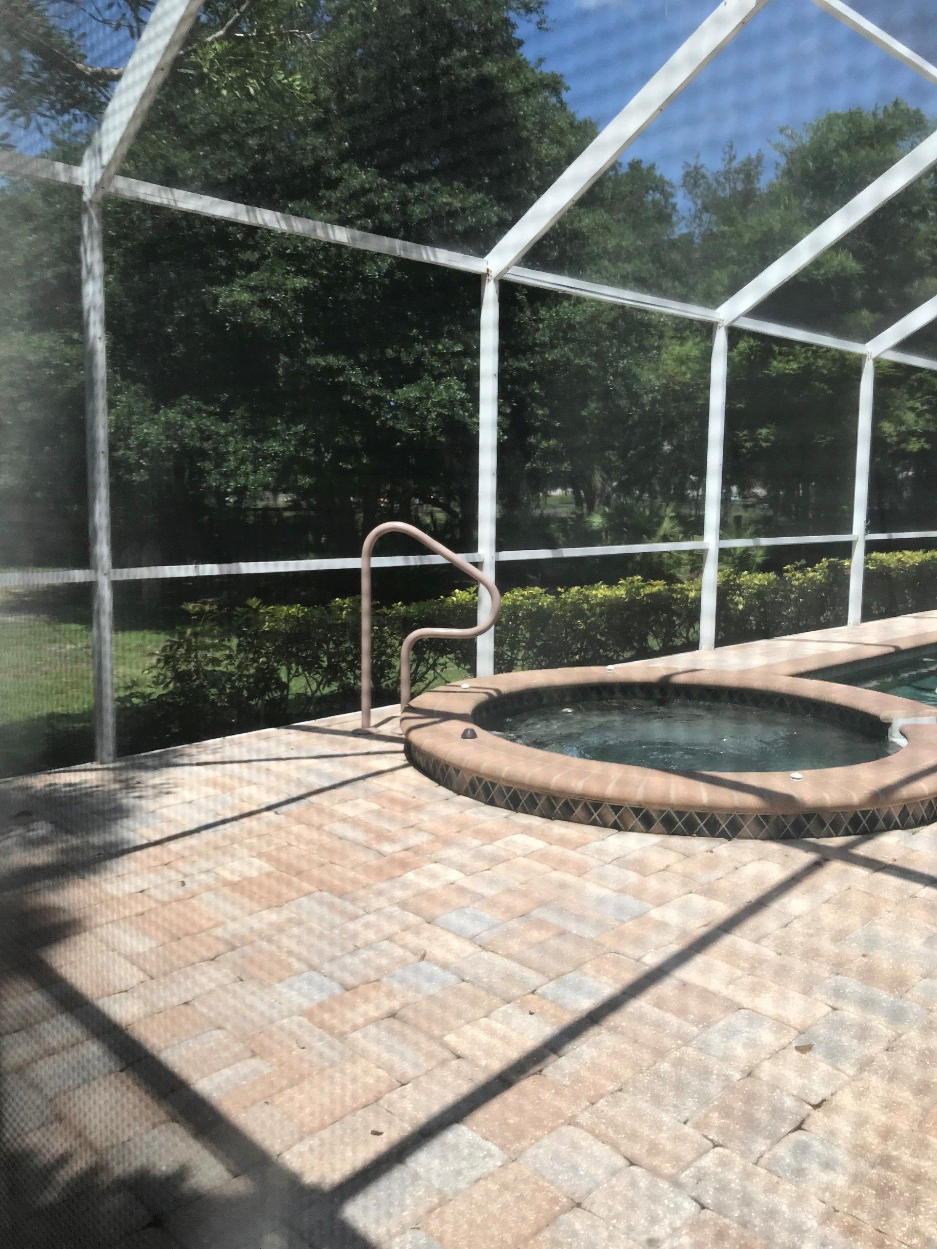 Screened pool area with brick patio, hot tub, and metal handrail in sunlight.