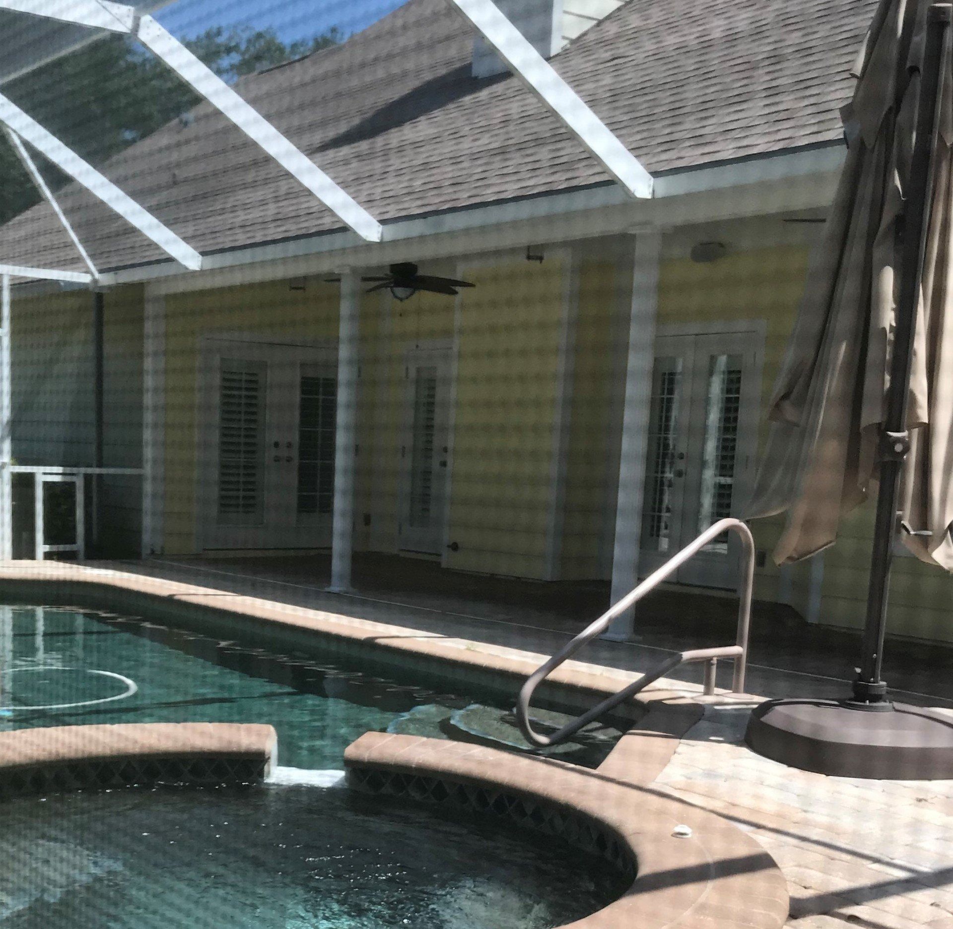 Backyard pool and screened patio with a yellow house and white support beams