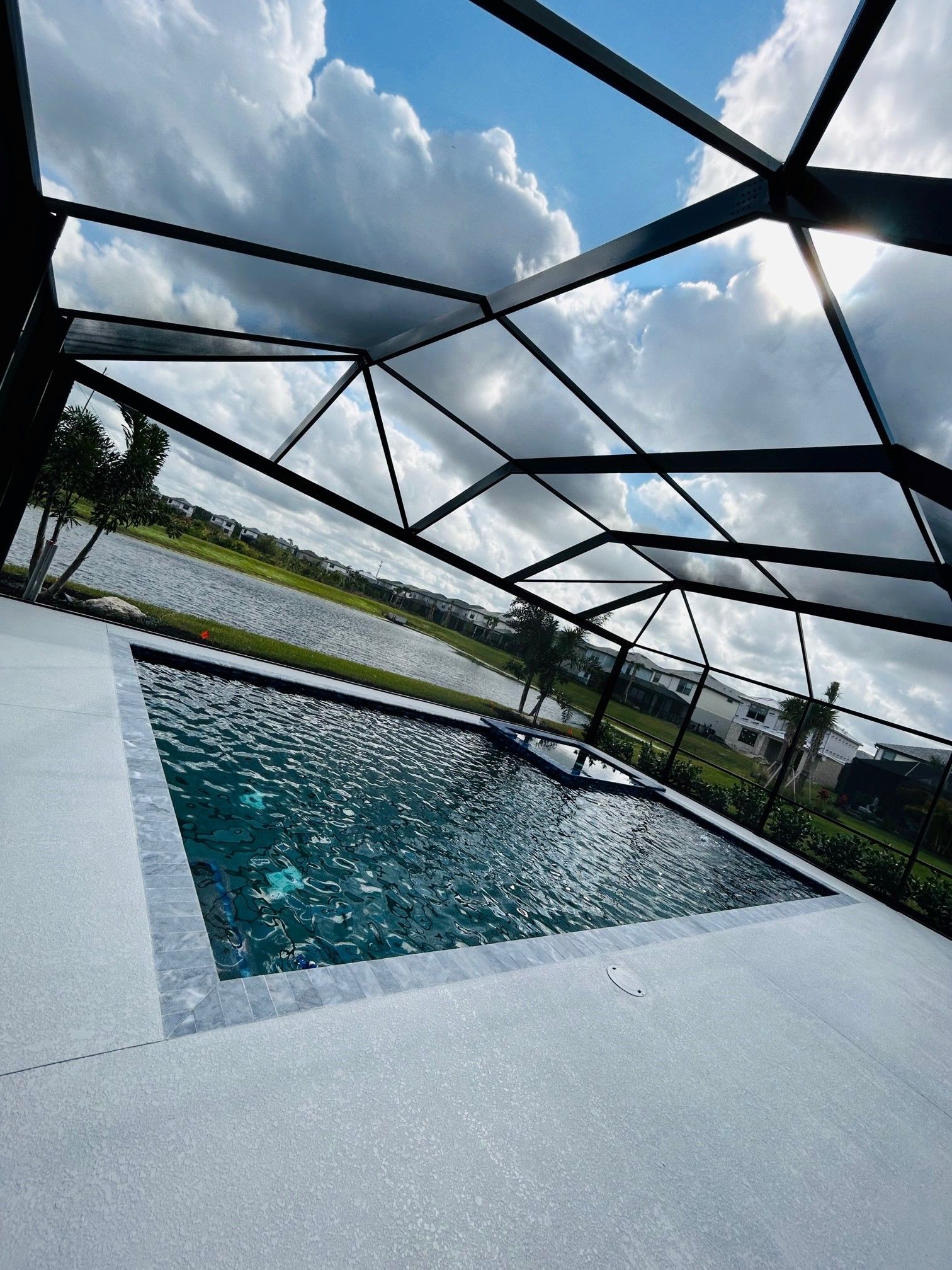 A rectangular pool enclosed by a black screen cage, overlooking a lake under a cloudy sky.
