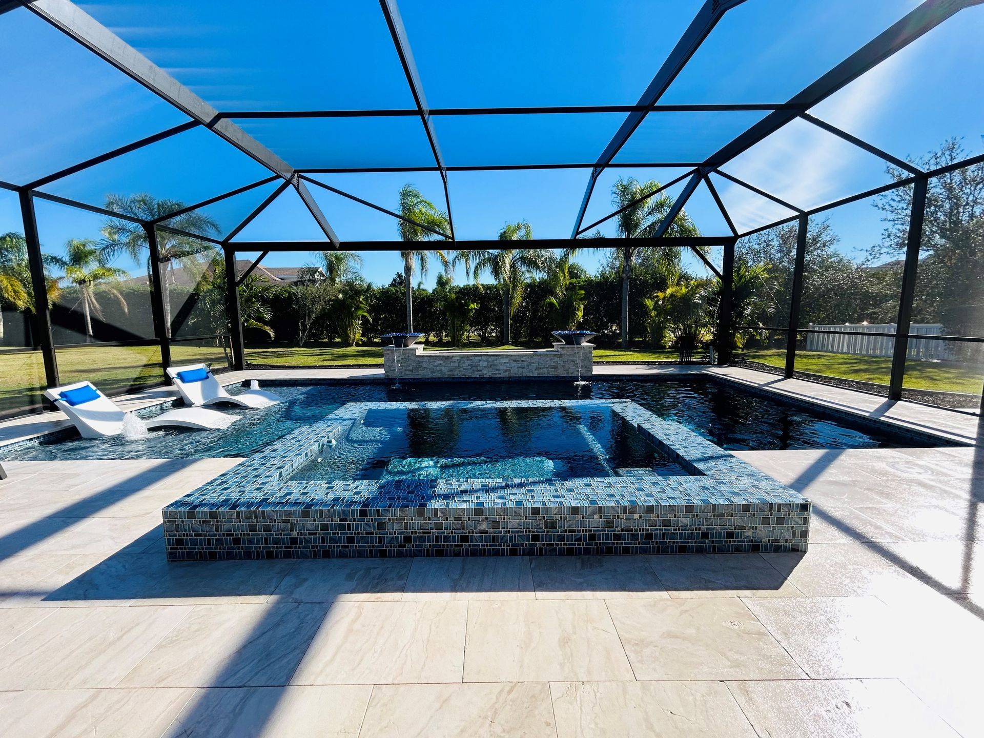 Covered backyard pool with blue water, white loungers, and a screened patio under a bright blue sky