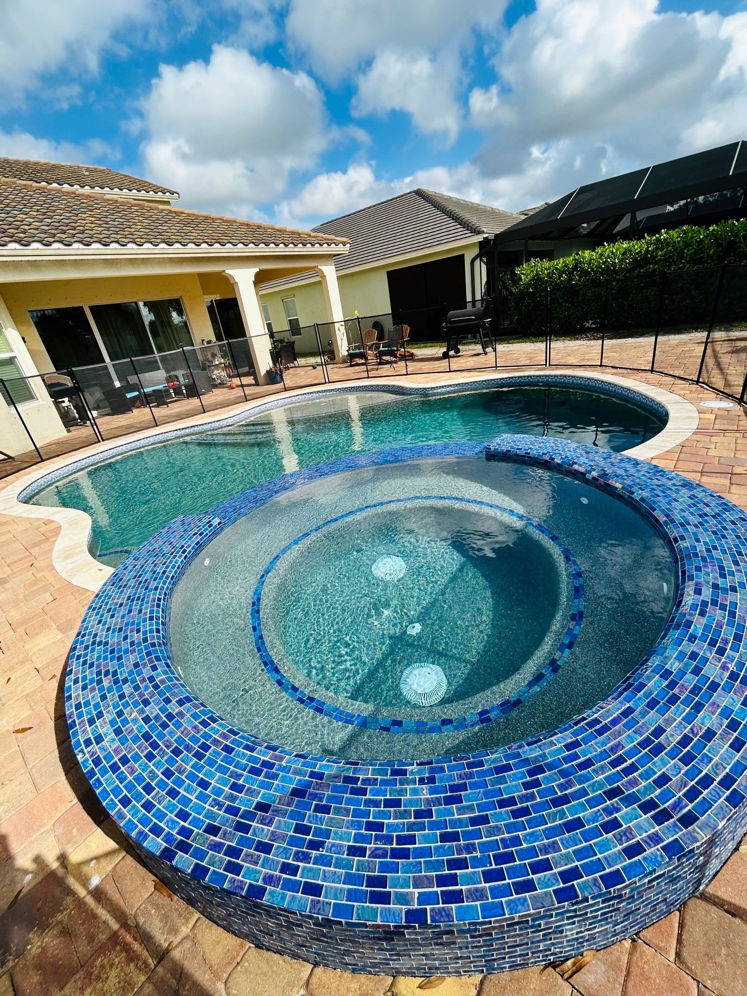 Backyard pool with a blue-tiled hot tub and surrounding patio beside a house