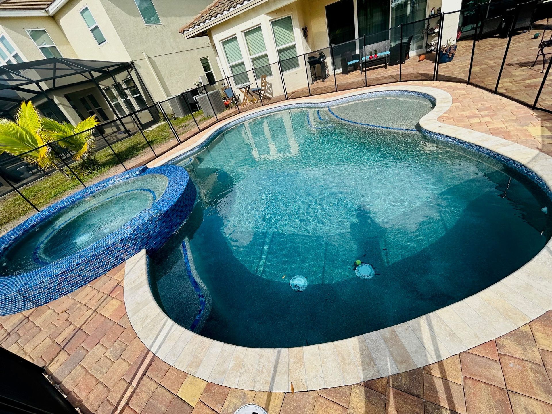 A backyard swimming pool with a connected raised circular spa and a paved deck, viewed from an elevated angle.