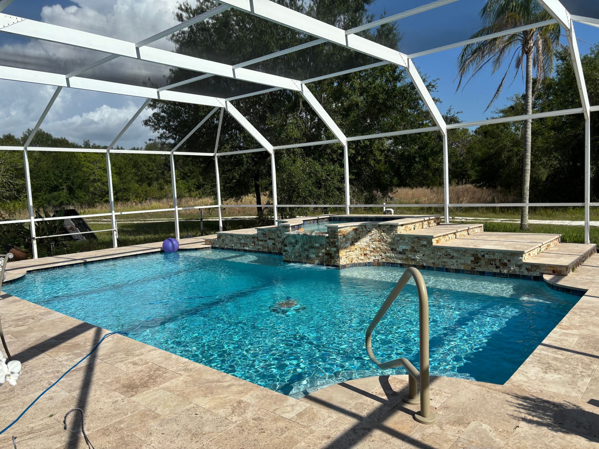 Screened backyard pool with blue water, stone deck, and white metal enclosure under a sunny sky
