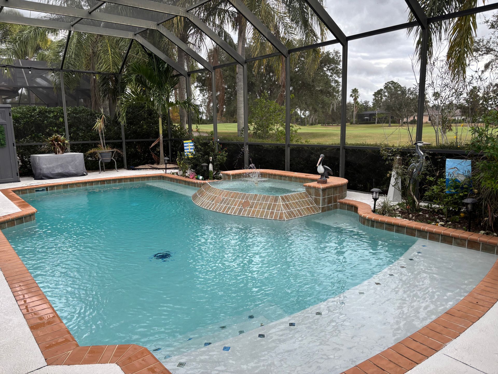 A swimming pool with an integrated spa, surrounded by a screened-in enclosure, with a green lawn in the background.