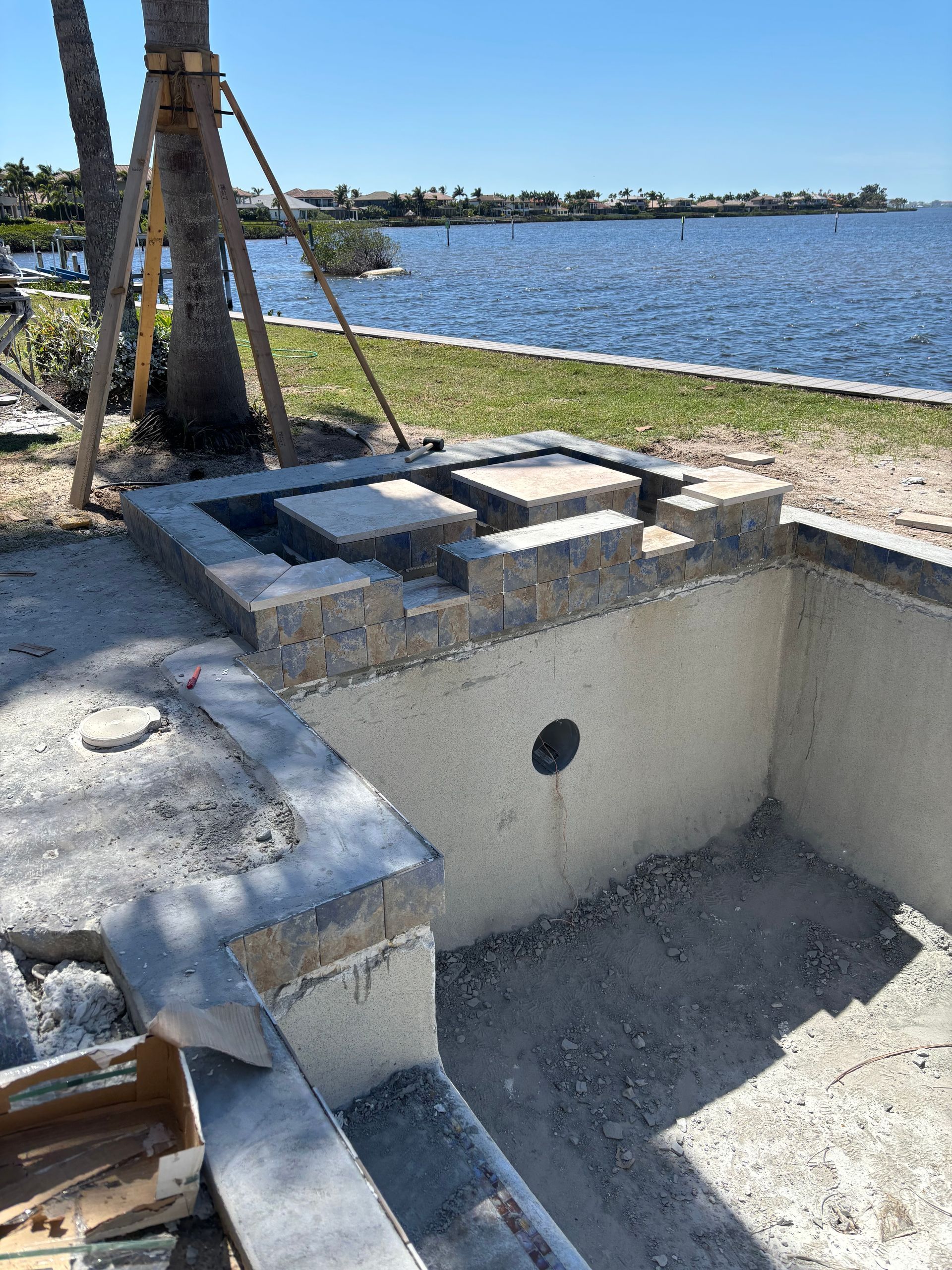 An unfinished concrete spa structure under construction, featuring stacked stone blocks and a view of a waterfront.