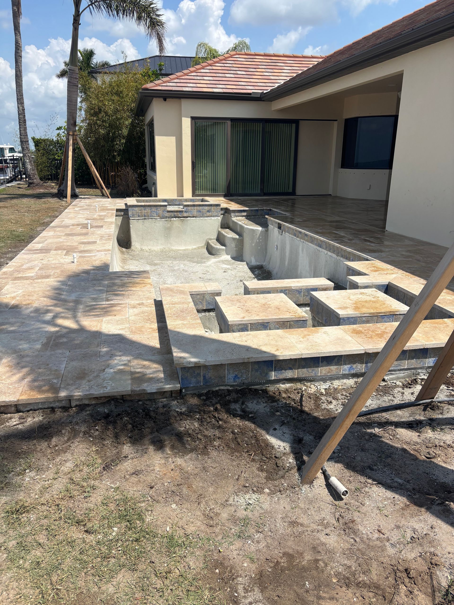 An unfinished swimming pool and patio area under construction outside a residential home.