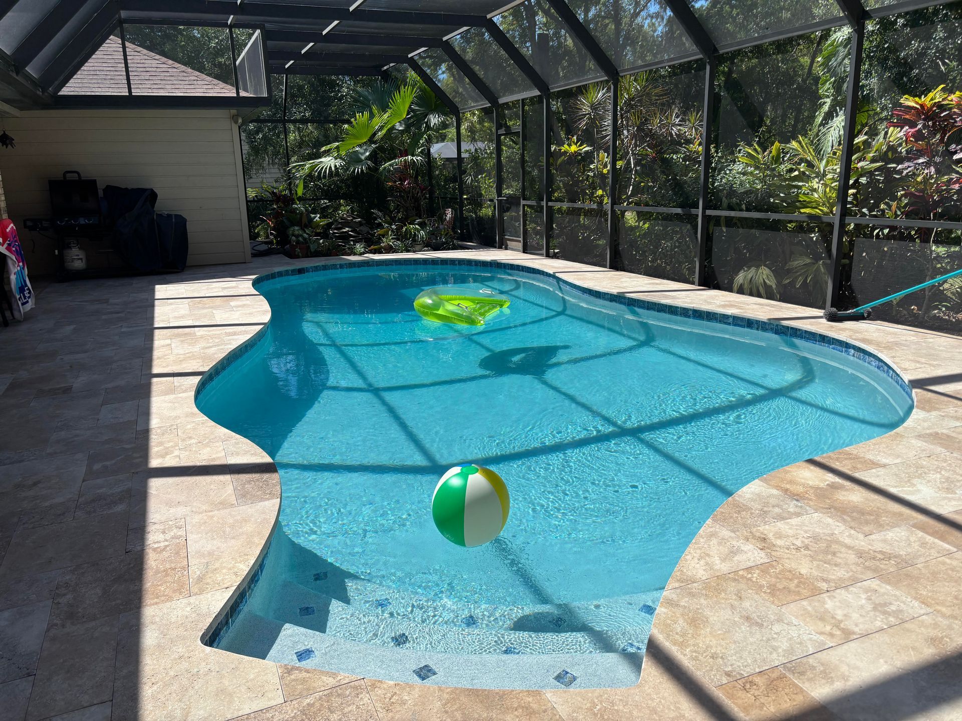 Covered backyard pool with a floating beach ball and pool float under a screened enclosure.