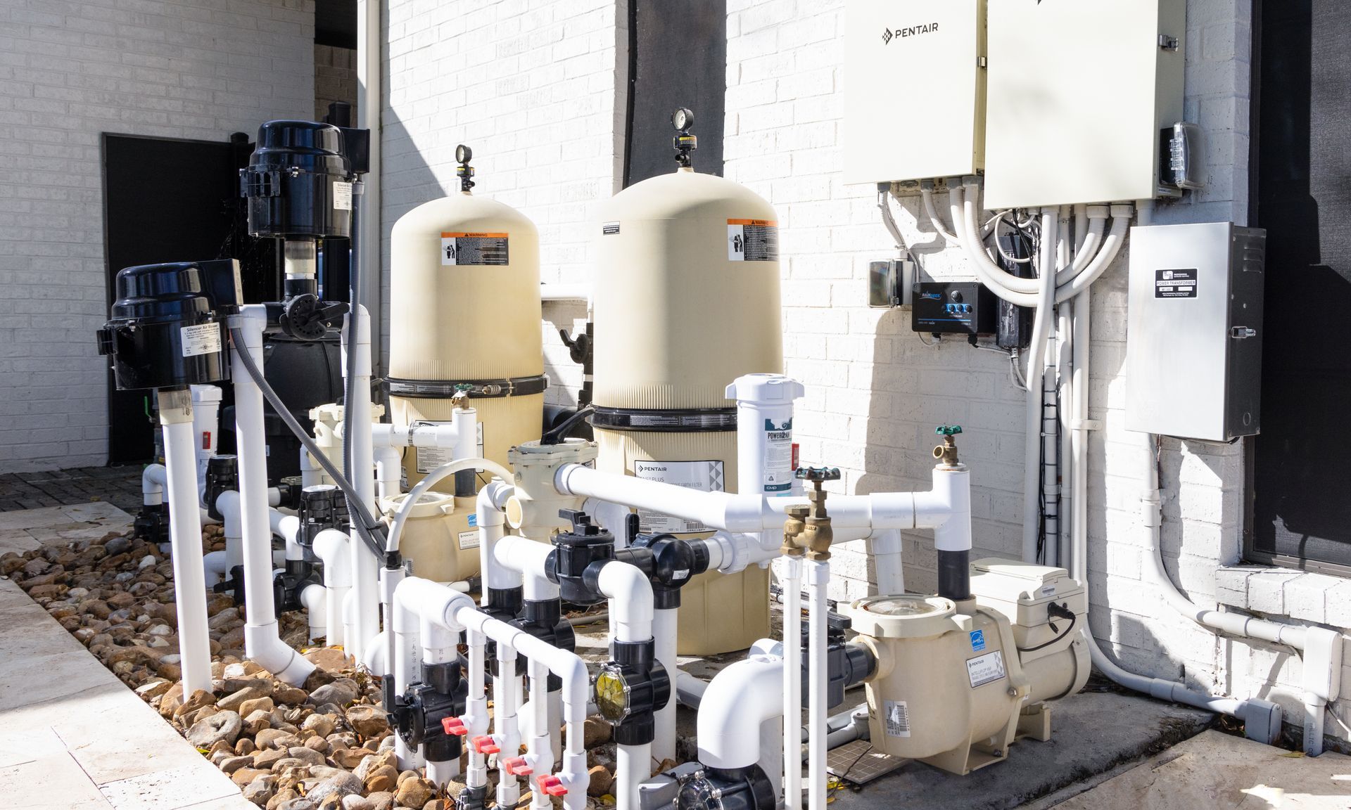 Outdoor utility equipment with beige tanks, pipes, and pumps beside a building wall