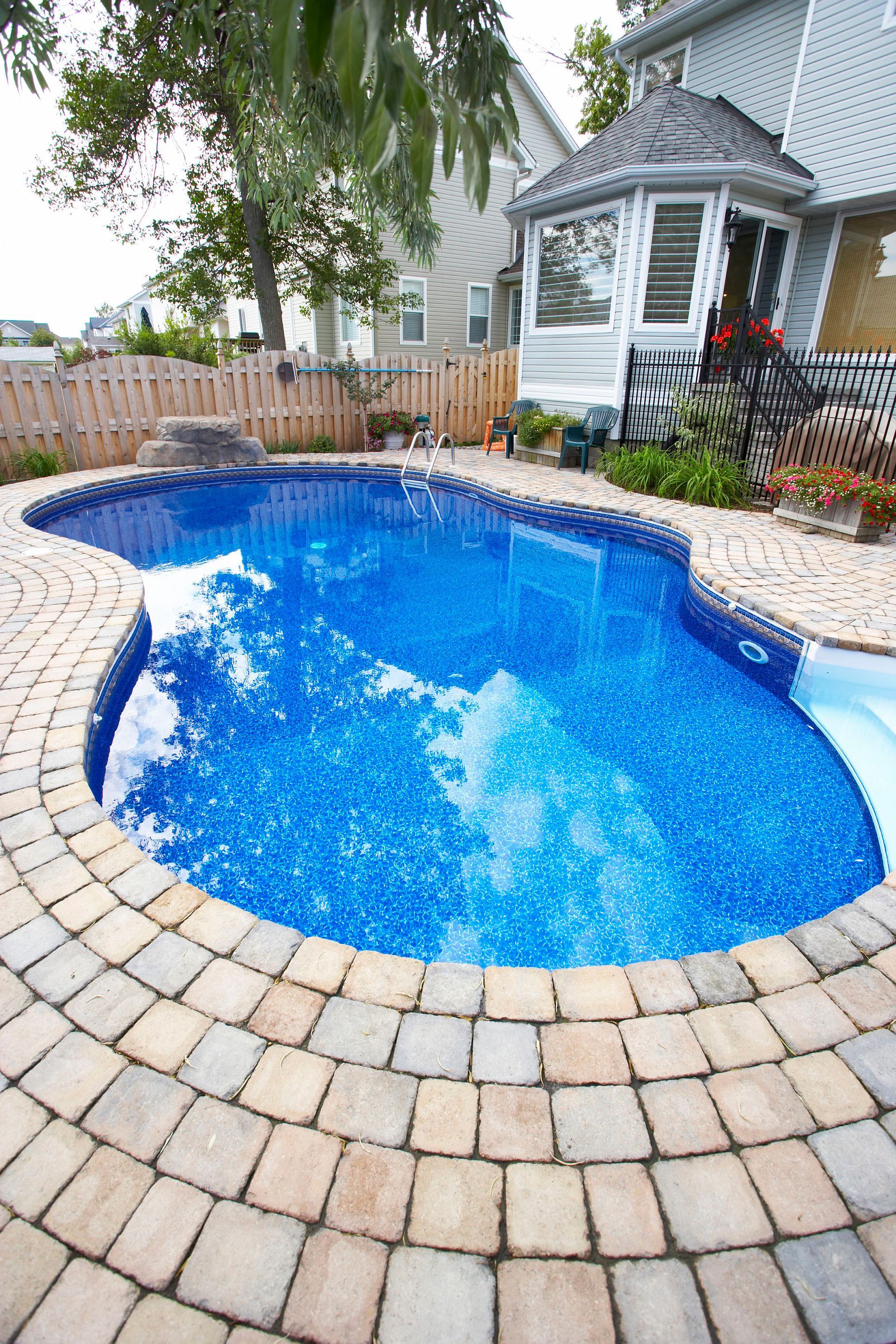 Curved backyard pool with blue water, stone pavers, and a house with a screened porch in the background