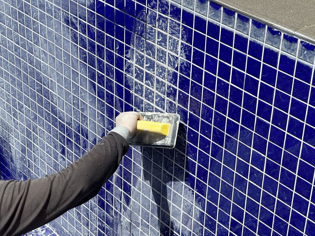Hand smoothing blue tiles with a yellow trowel on a tiled wall