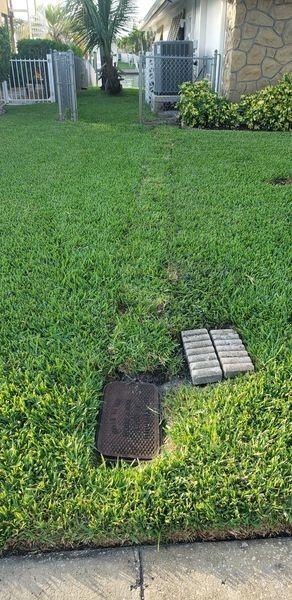 A manhole cover is sitting in the grass in front of a house.
