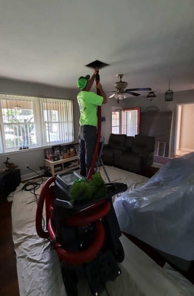A man is cleaning the ceiling of a living room with a vacuum cleaner.