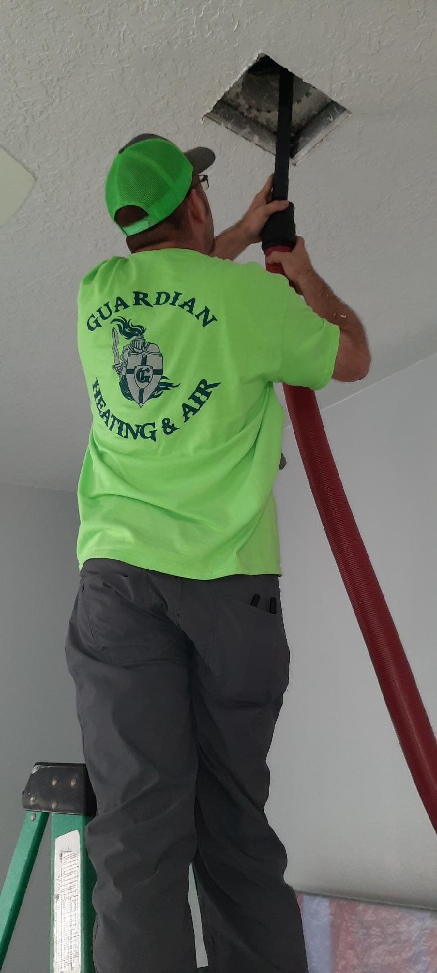 A man in a green shirt is standing on a ladder cleaning a ceiling.