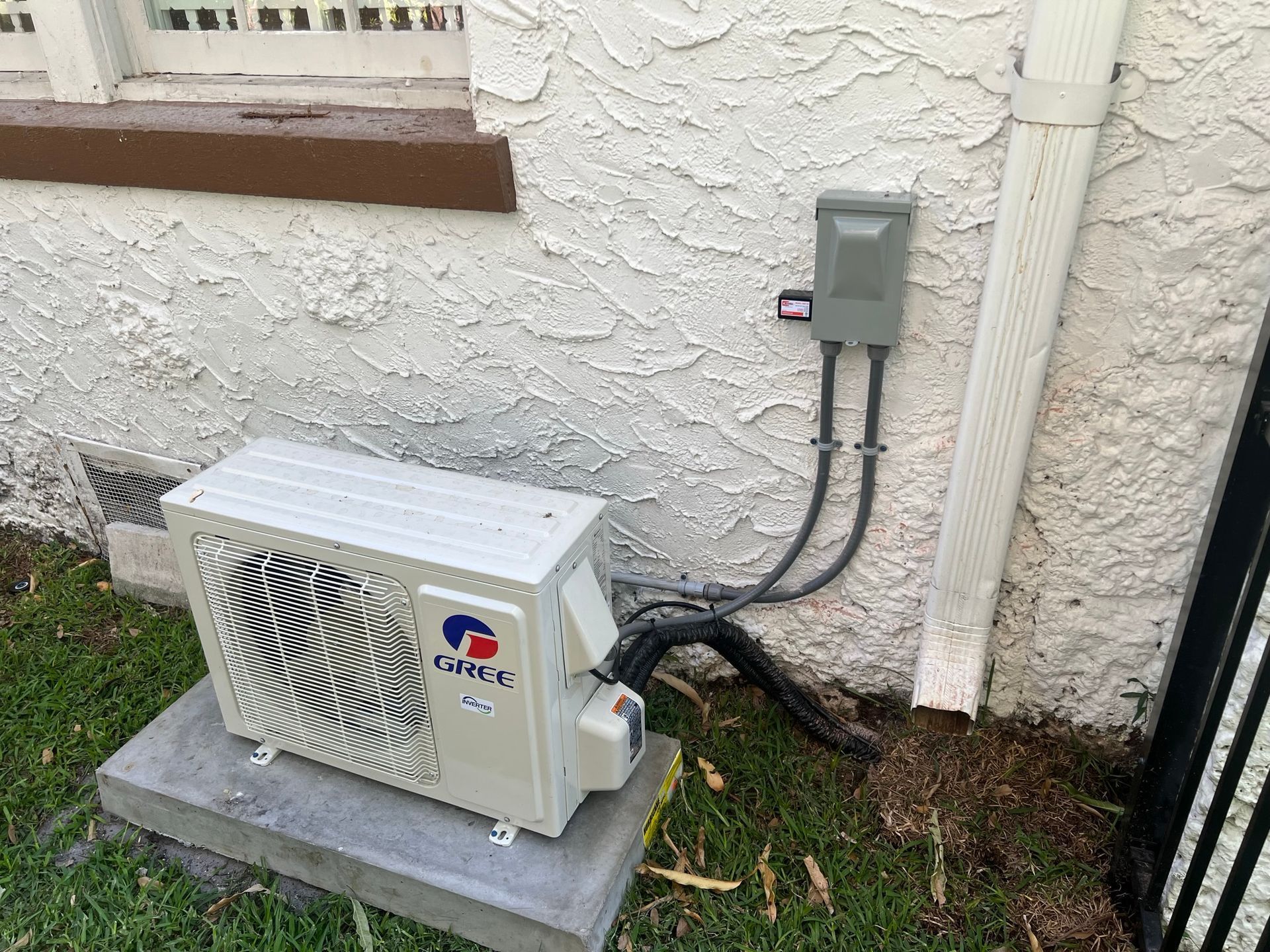 A white air conditioner is sitting on top of a concrete block next to a building.