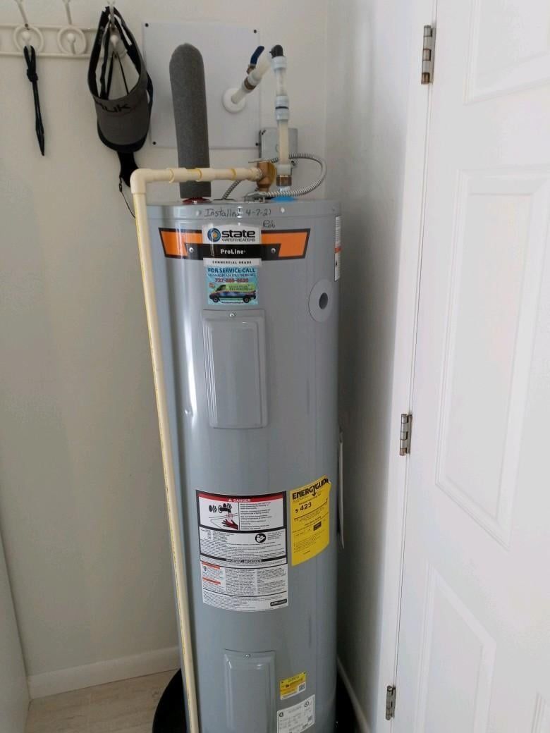 A water heater is sitting in a corner of a room next to a door.