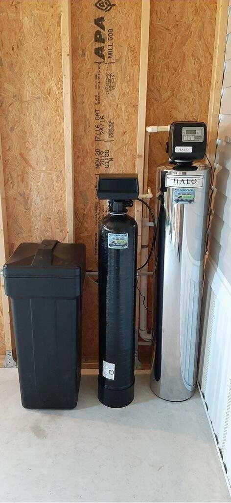 A water softener is sitting next to a trash can in a room.