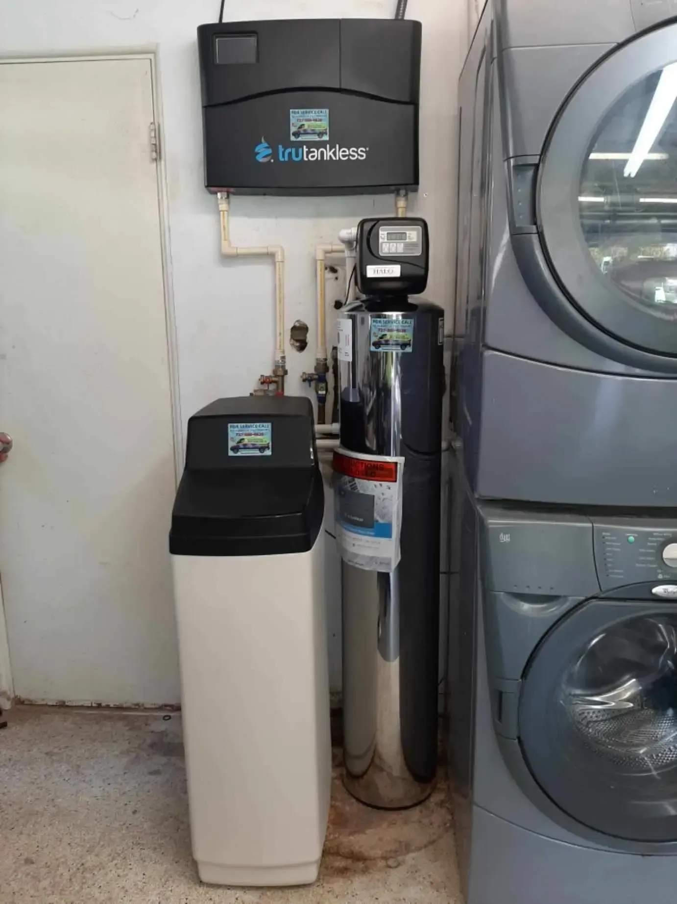 A water softener is sitting next to a washer and dryer in a laundromat.