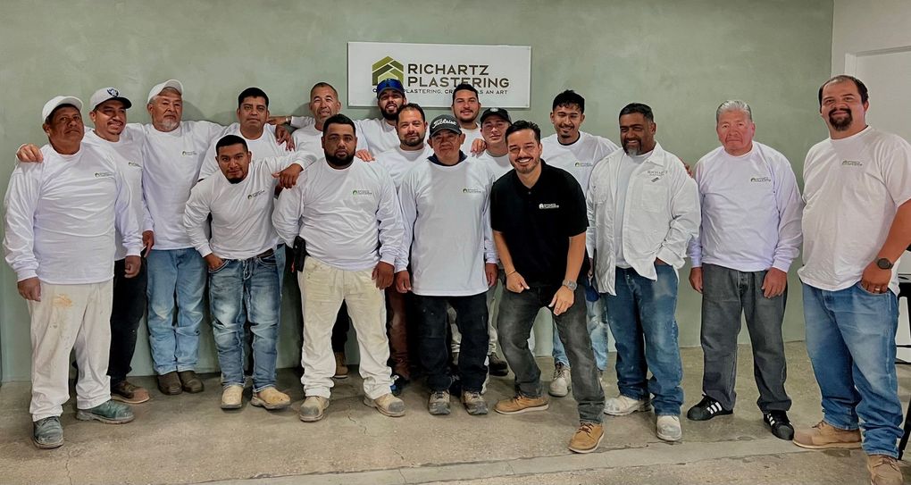 Group of people in white shirts and jeans posing indoors in front of a wall banner.