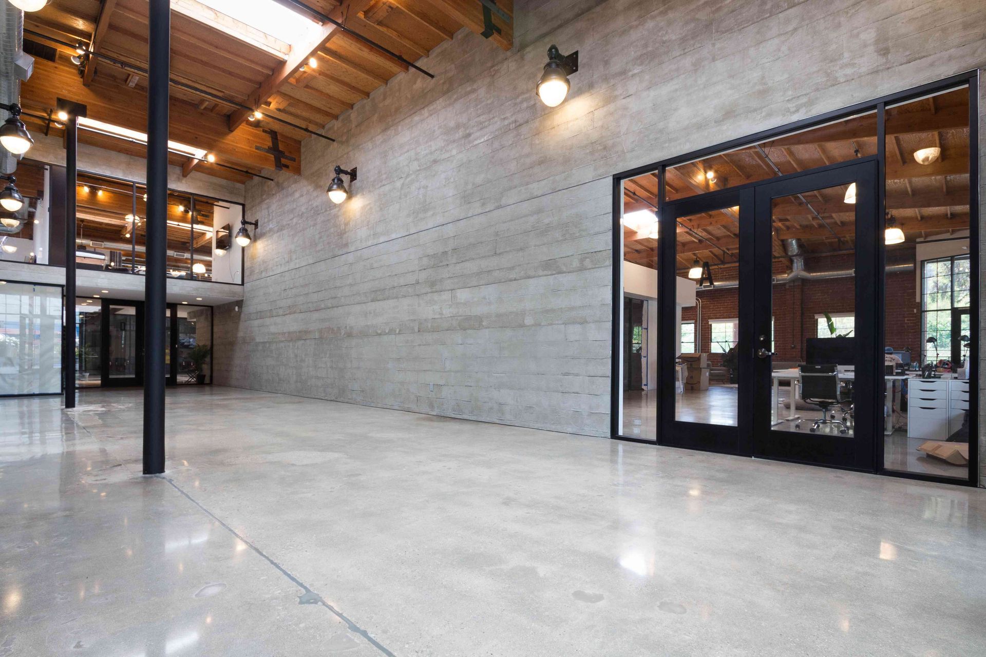Spacious modern industrial loft with concrete floors, wood ceiling beams, and large glass-walled offices.