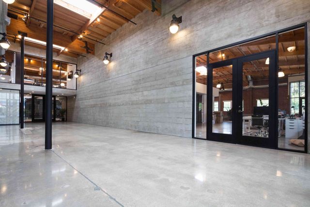 Spacious modern industrial interior with concrete floors, exposed wood beams, and glass-walled rooms