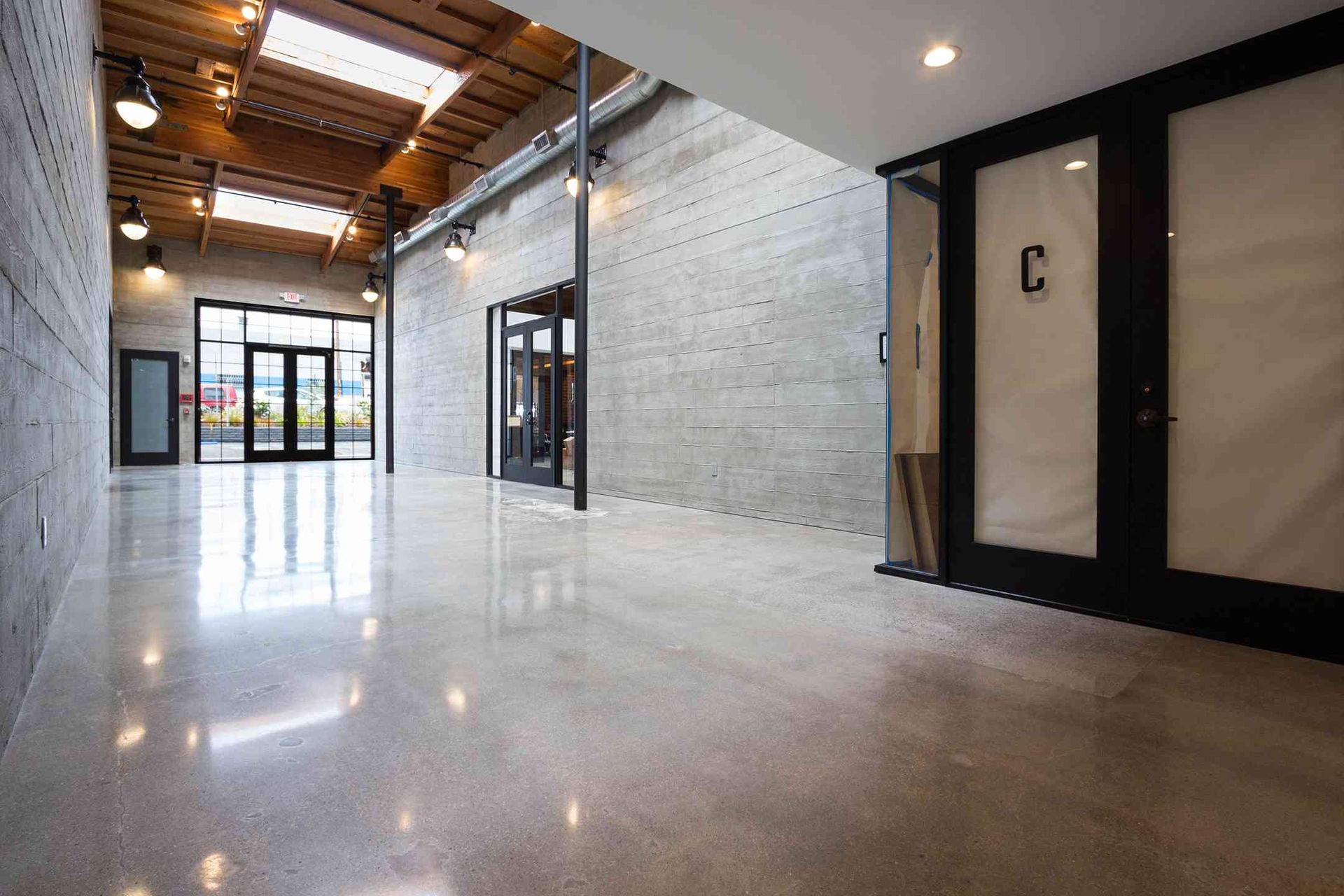 Modern industrial hallway with polished concrete floors, exposed wood beams, white brick walls, and glass doors