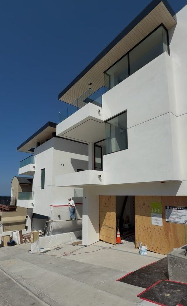 Modern white multi-story townhouse under construction with boarded ground-floor openings and a clear blue sky