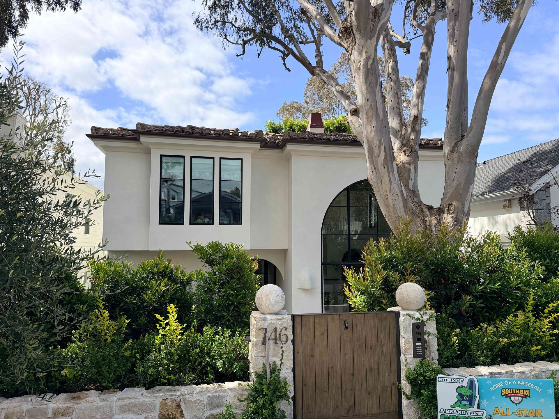 Modern white stucco house with arched entry, black windows, and a wooden gate behind a stone wall.