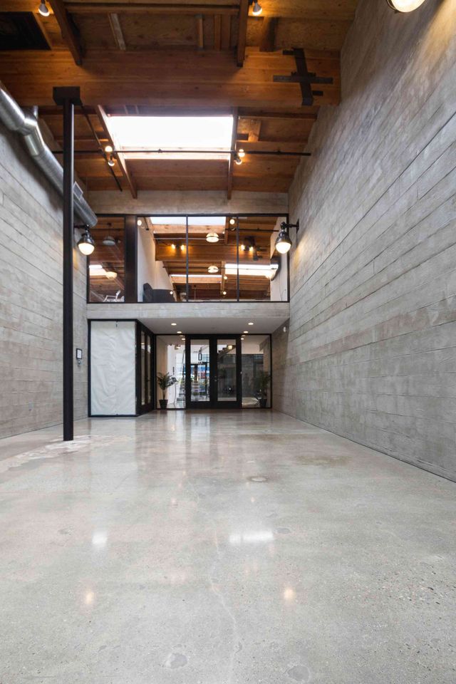 Spacious modern lobby with polished concrete floor, wood ceiling, glass entrance, and tall concrete wall