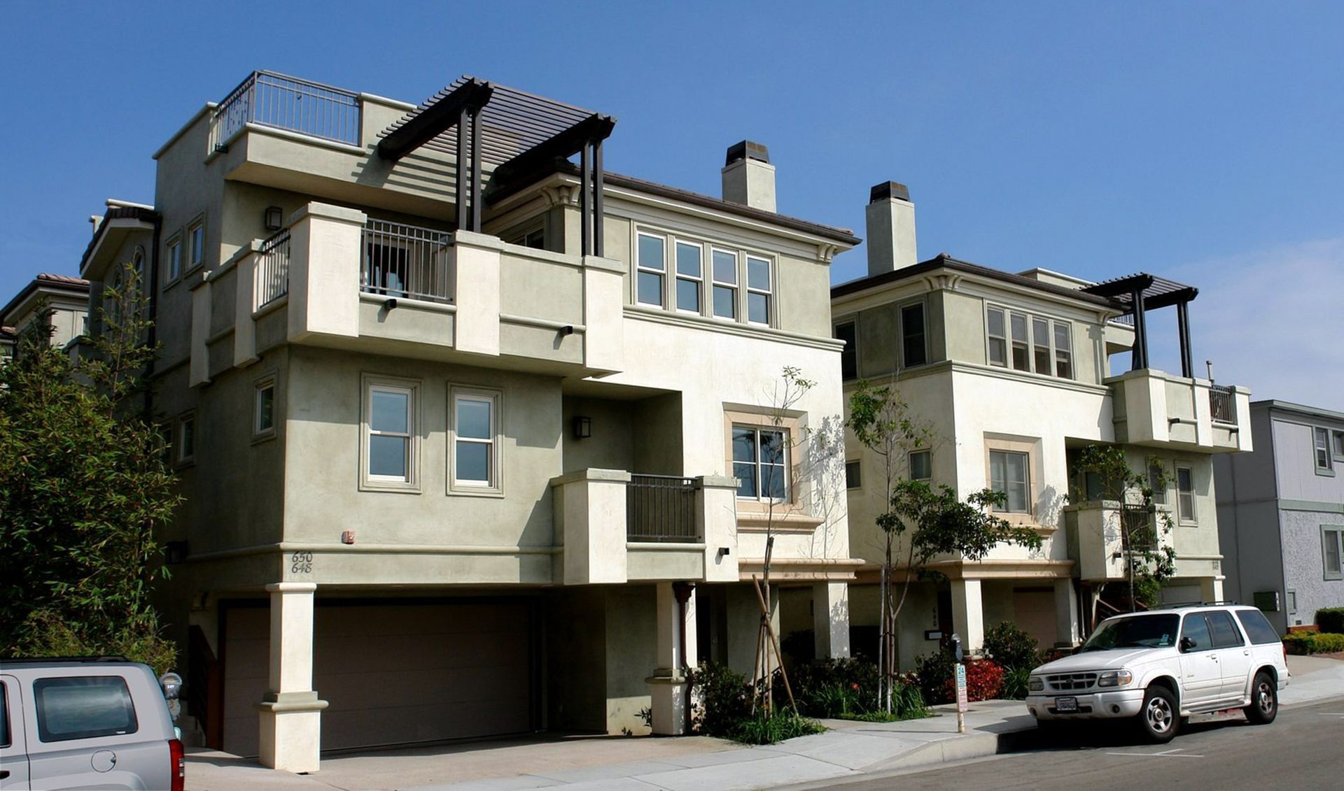 Row of modern apartment buildings with balconies and parked cars on a sunny street