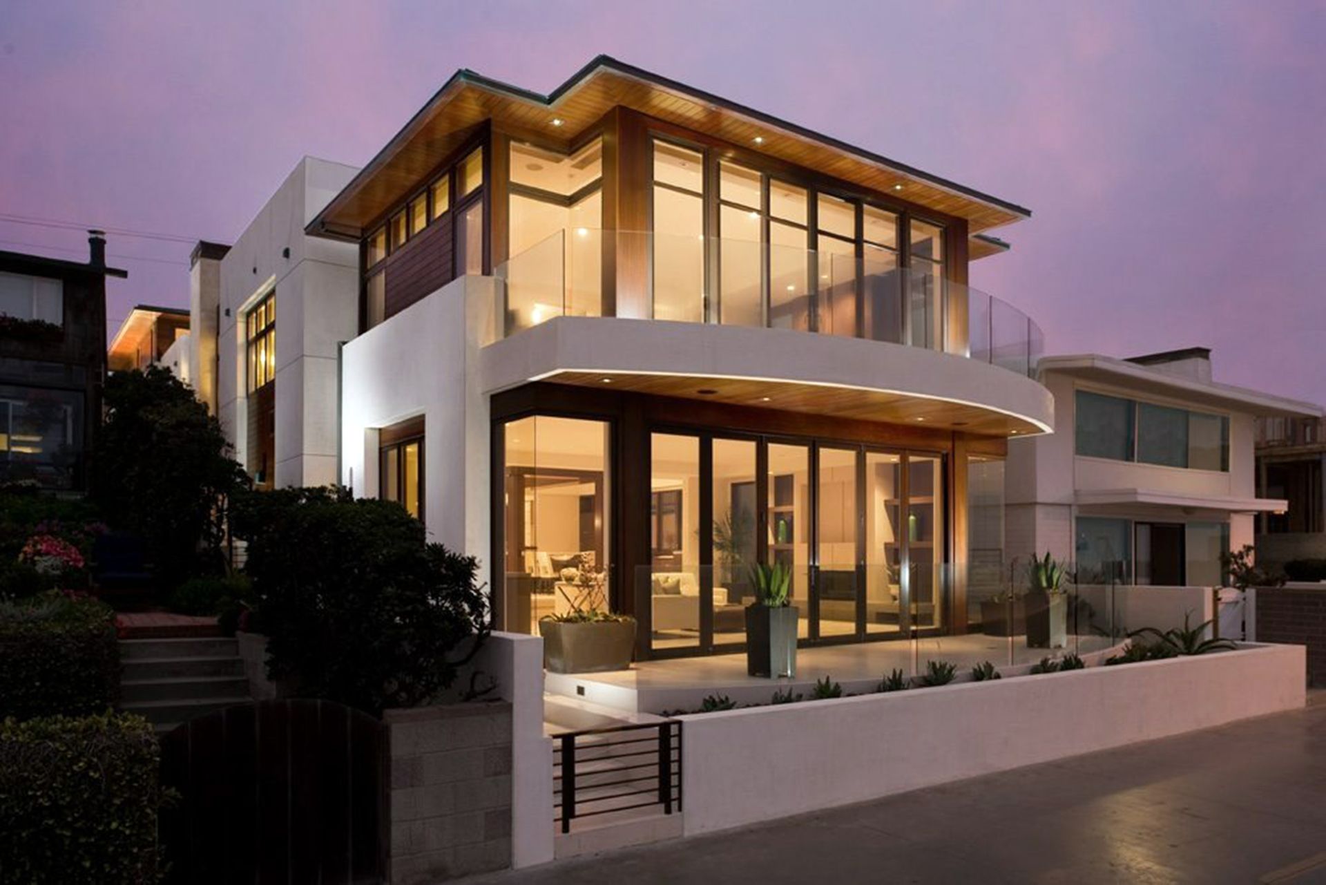 Modern two-story house with large glass windows and warm interior lights at dusk