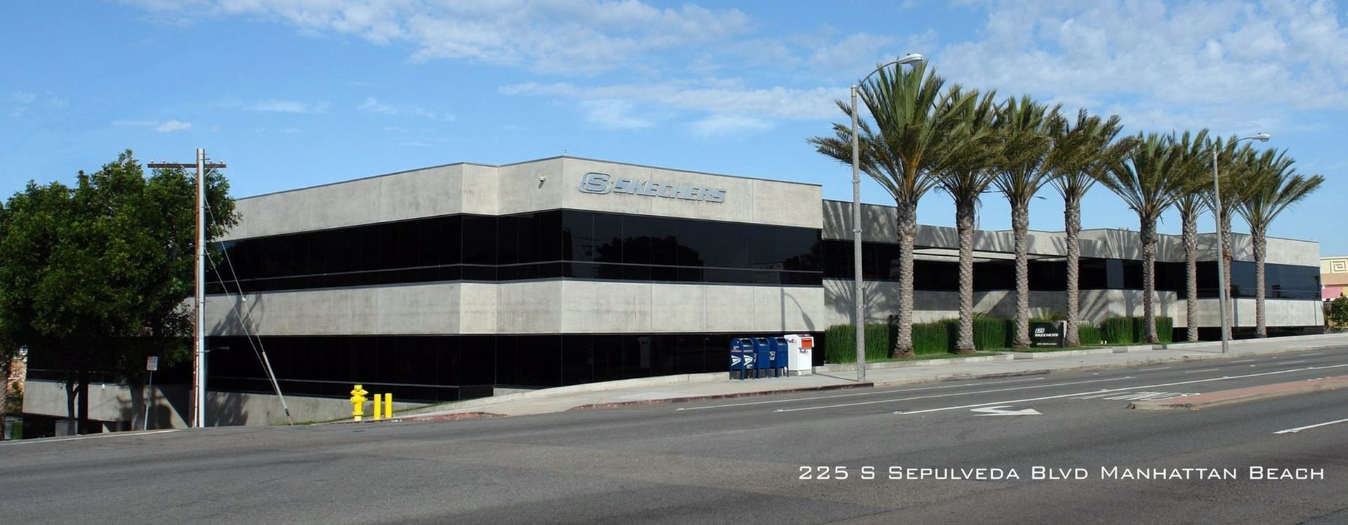 Modern two-story office building with black-and-white facade, palm trees, and a parking lot under a clear blue sky