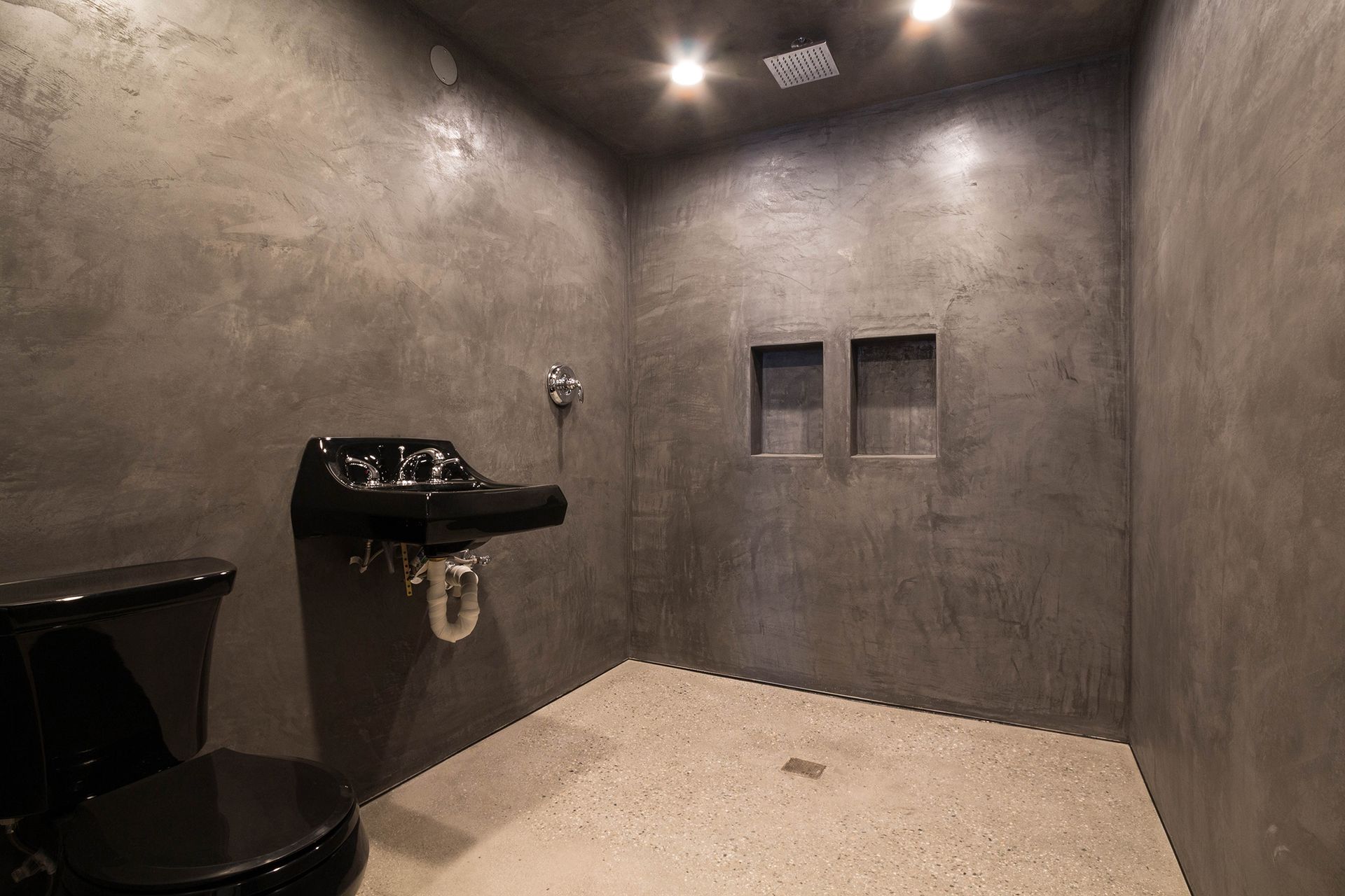 Dark tiled public restroom with a black sink, toilet, and two wall-mounted urinals.