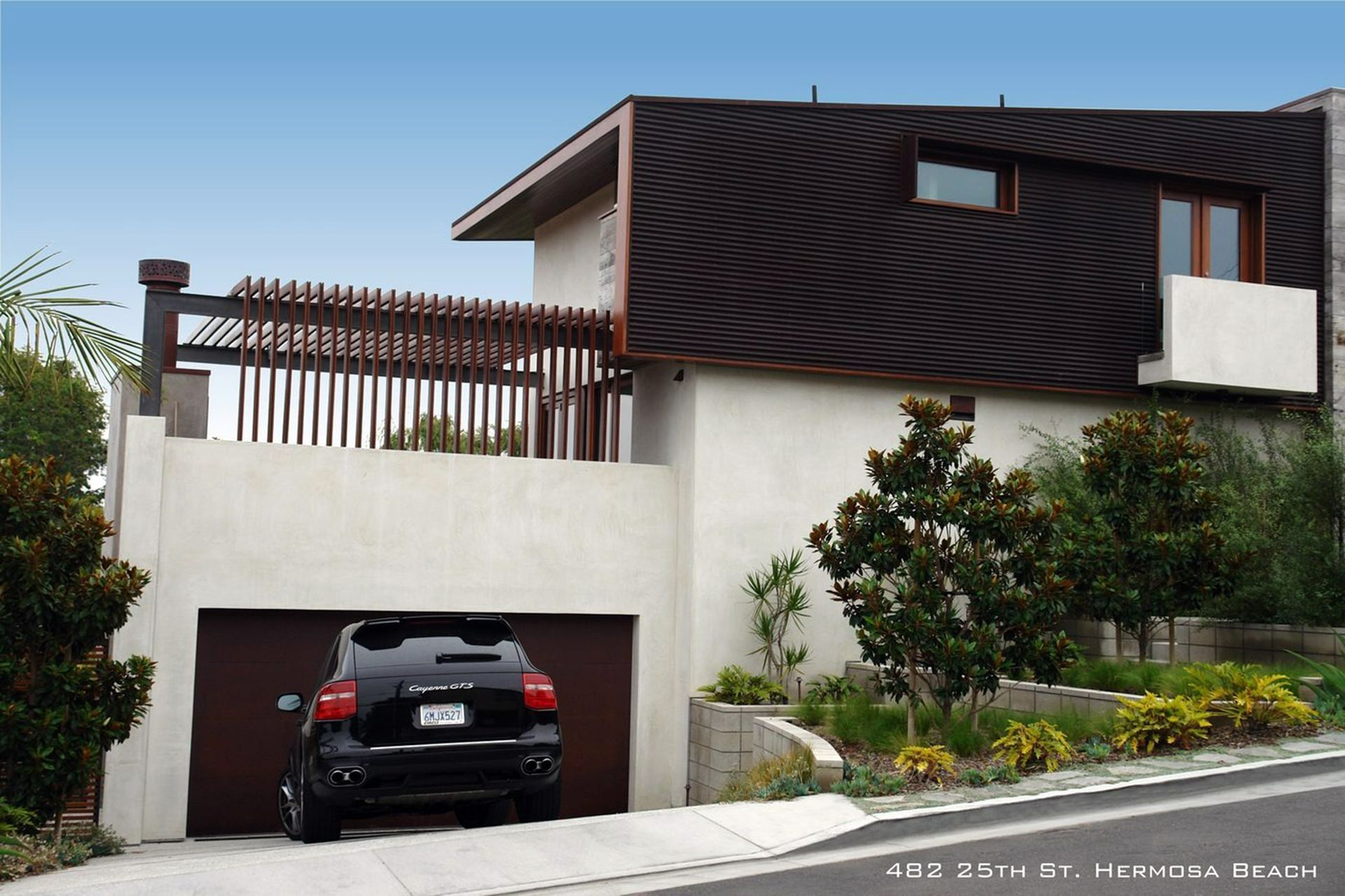 Modern hillside house with dark upper facade, white lower level, and a black SUV in the garage