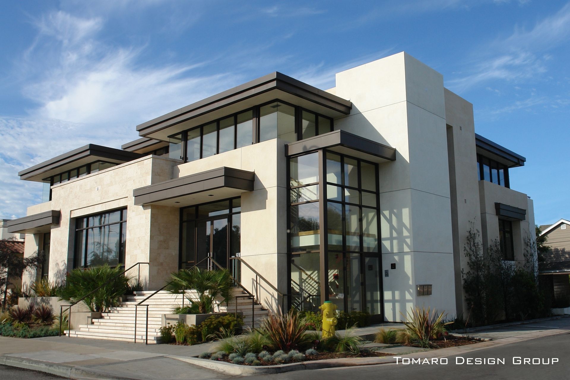 Modern two-story house with large windows, stone facade, and landscaped front entrance under a blue sky