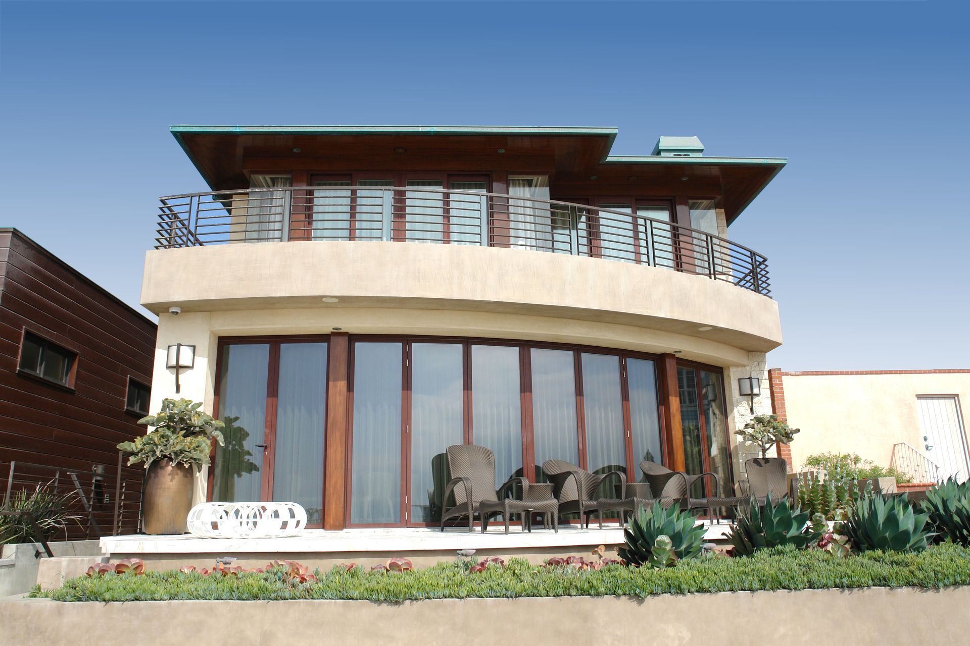 Modern two-story house with curved glass facade, balcony, and landscaped front yard