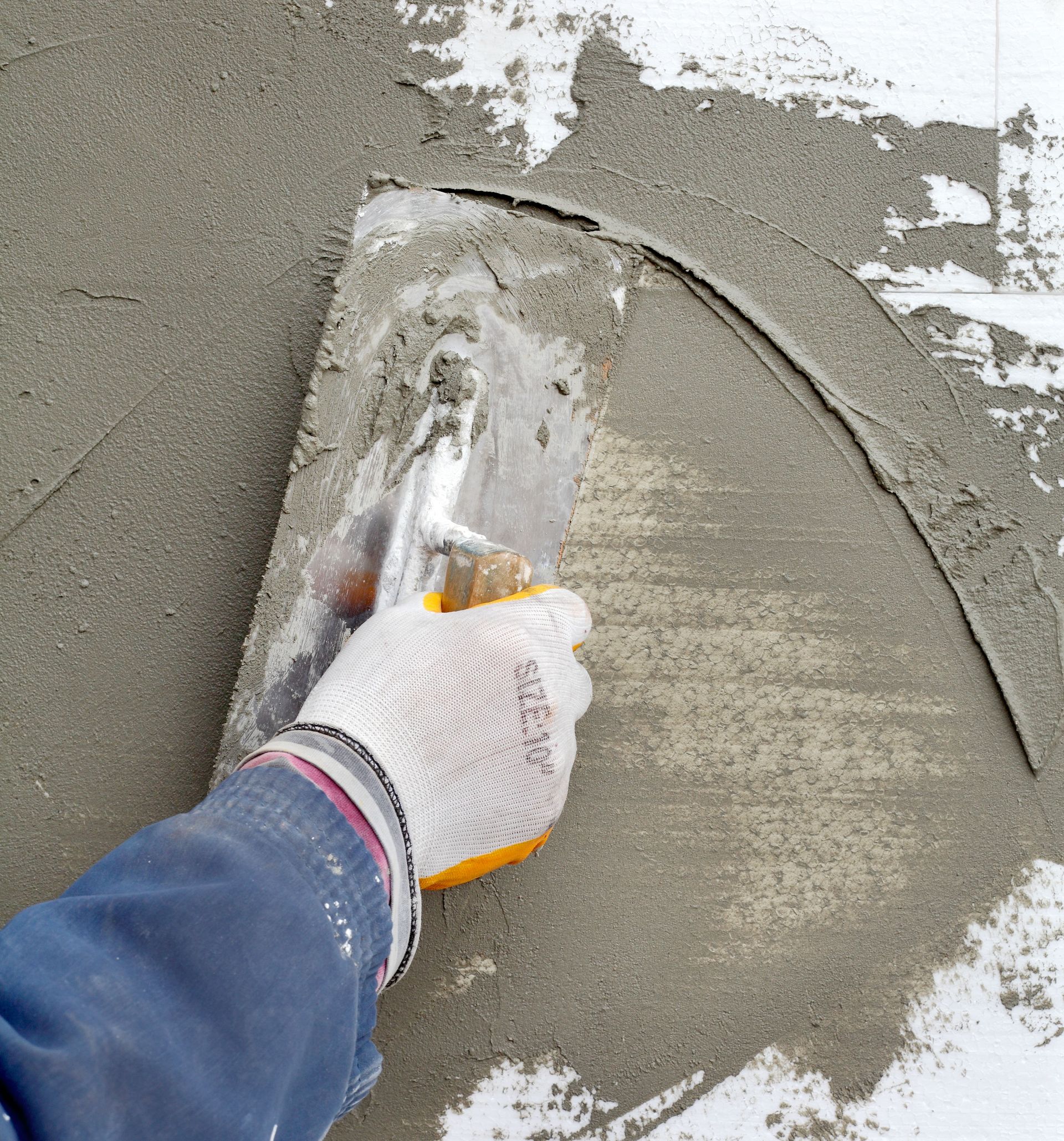 Gloved hand smoothing gray plaster on a wall with a trowel