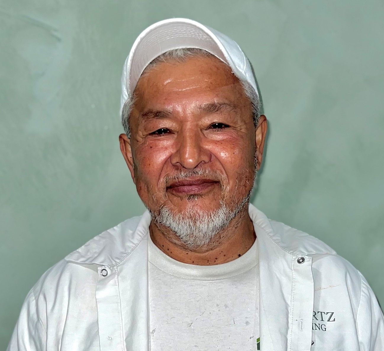 Smiling man in a white cap and jacket against a plain green background