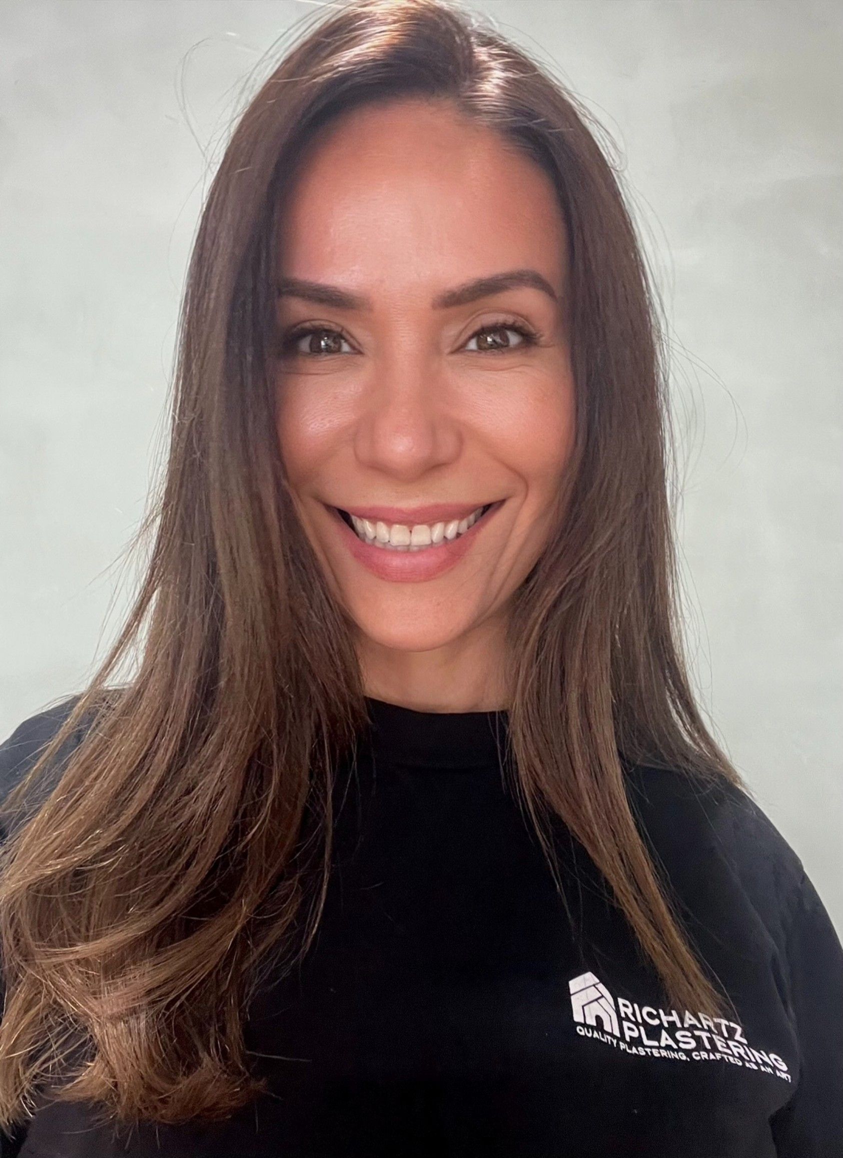 Smiling woman with long dark hair wearing a black shirt against a light background
