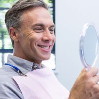 A man is smiling while looking at his teeth in a mirror.